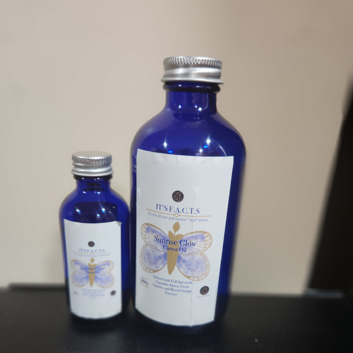 2oz and 8oz cobalt blue bottles of Sunrise glow carrot hair oil